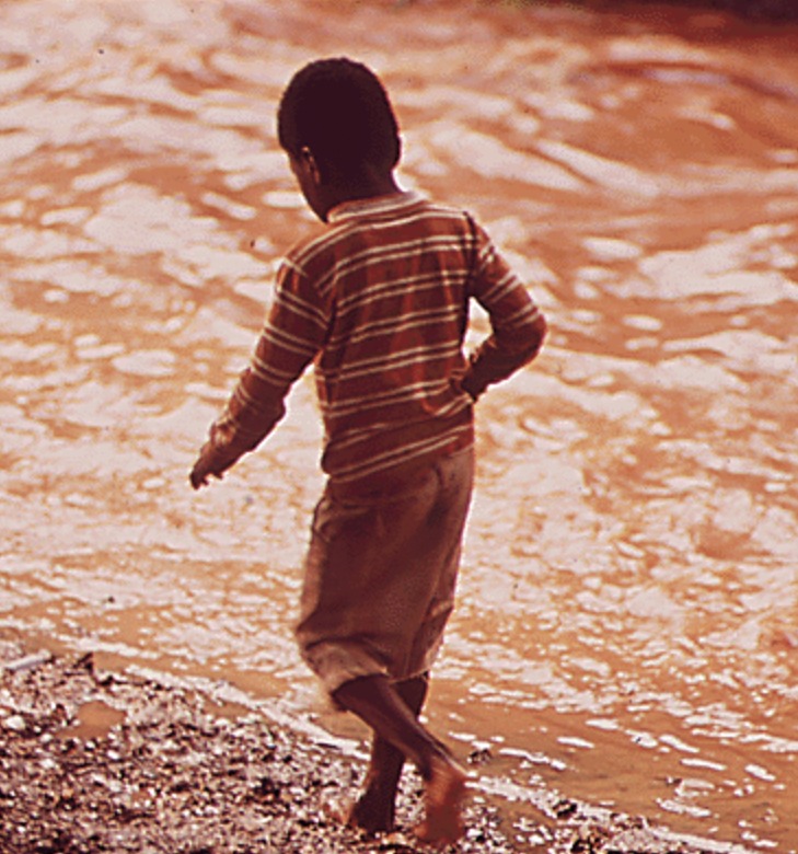 Boy Walks Along Creek Polluted by Steel Mill Effluent.png
